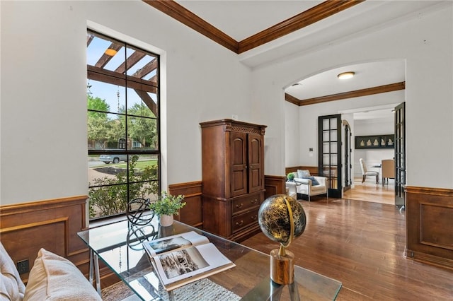 dining room with a wainscoted wall, wood finished floors, arched walkways, and crown molding