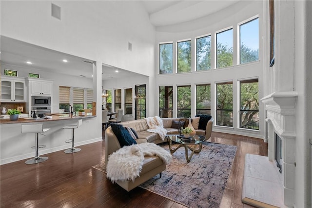 living area with a fireplace, a high ceiling, baseboards, and wood-type flooring