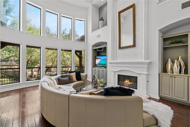 living area with a healthy amount of sunlight, a fireplace, visible vents, and dark wood-type flooring