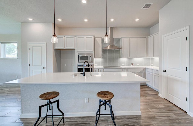 kitchen with a sink, stainless steel appliances, tasteful backsplash, wood finished floors, and wall chimney exhaust hood