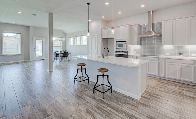 kitchen with oven, white cabinetry, white microwave, wall chimney range hood, and tasteful backsplash