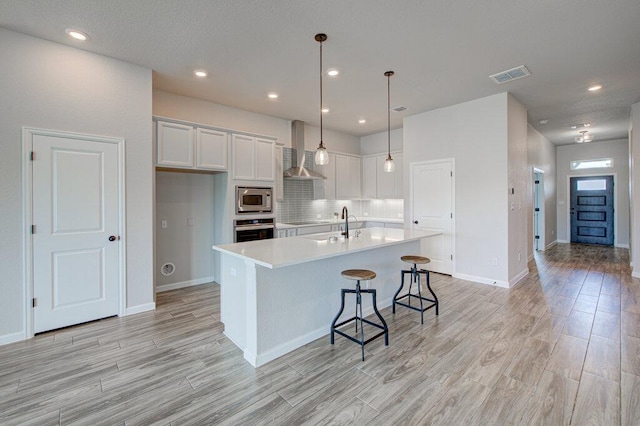 kitchen featuring light wood-type flooring, visible vents, wall chimney exhaust hood, white cabinetry, and appliances with stainless steel finishes