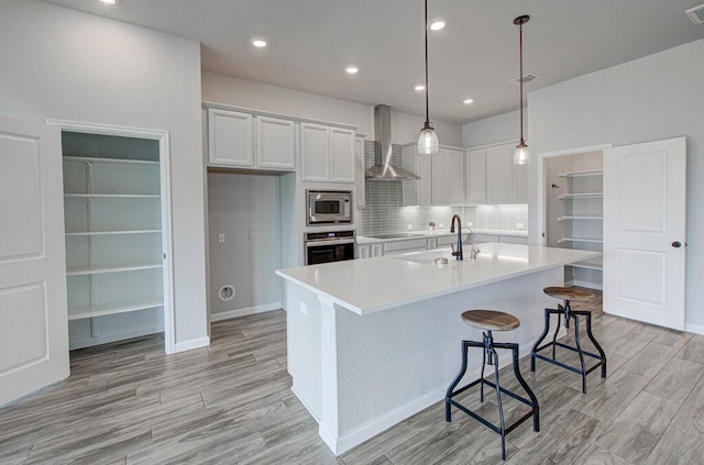kitchen with visible vents, a sink, white cabinetry, wall chimney range hood, and stainless steel appliances