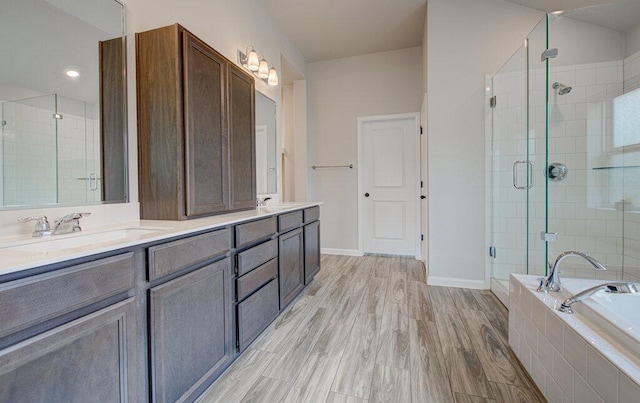 bathroom with double vanity, a garden tub, a stall shower, a sink, and baseboards