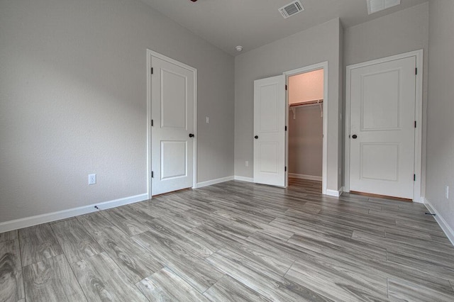 unfurnished bedroom with a closet, baseboards, visible vents, wood finished floors, and a spacious closet