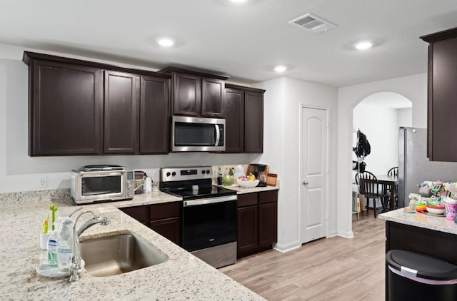 18720 Speculator Ln, Elgin, TX 78621 - kitchen with a sink, a toaster, dark brown cabinetry, arched walkways, and appliances with stainless steel finishes