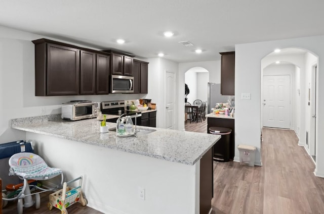 18720 Speculator Ln, Elgin, TX 78621 - kitchen with light wood-type flooring, visible vents, arched walkways, dark brown cabinets, and appliances with stainless steel finishes