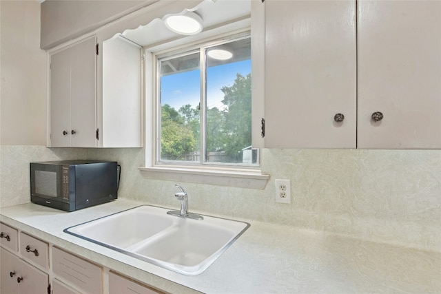 7000 Miranda Dr, Austin, TX 78752 - kitchen featuring black microwave, light countertops, backsplash, and white cabinetry