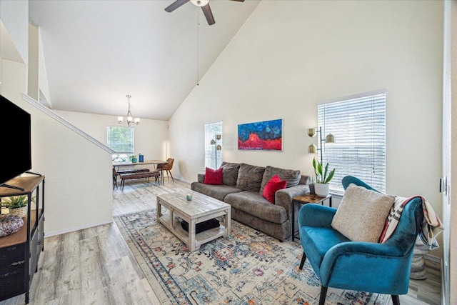 living area with ceiling fan with notable chandelier, high vaulted ceiling, and wood finished floors