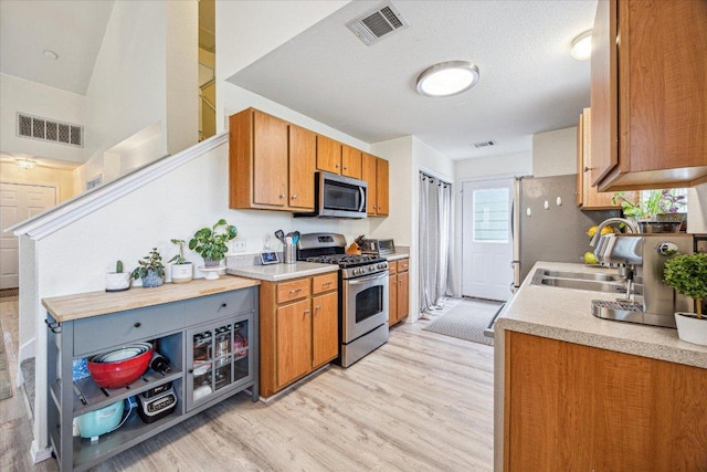 kitchen featuring brown cabinets, light wood-style floors, stainless steel appliances, and visible vents