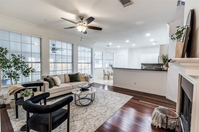living room featuring a fireplace, crown molding, dark wood-type flooring, visible vents, and ceiling fan