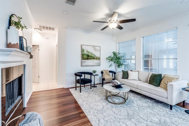 living area with a ceiling fan, crown molding, visible vents, and wood finished floors