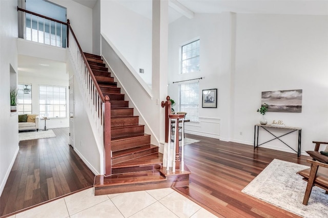 staircase featuring beamed ceiling, hardwood / wood-style flooring, a healthy amount of sunlight, and high vaulted ceiling