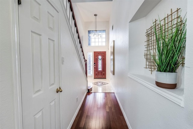 corridor featuring a notable chandelier, dark wood-style floors, baseboards, stairway, and a high ceiling