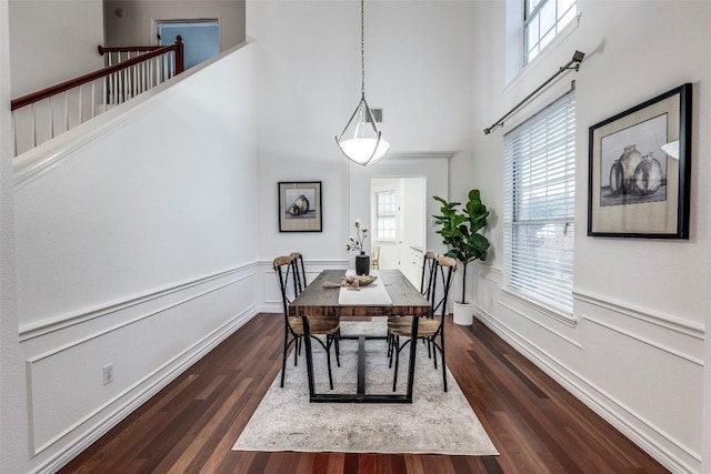 dining room featuring dark wood-style flooring, a high ceiling, and a wainscoted wall