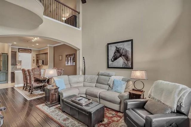 living area with wood finished floors, crown molding, ceiling fan, arched walkways, and a high ceiling