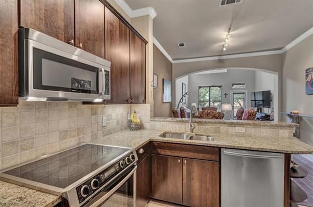 kitchen featuring a peninsula, a sink, stainless steel appliances, crown molding, and arched walkways
