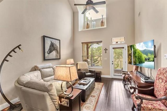 living area with baseboards, dark wood-style flooring, ceiling fan, and a high ceiling