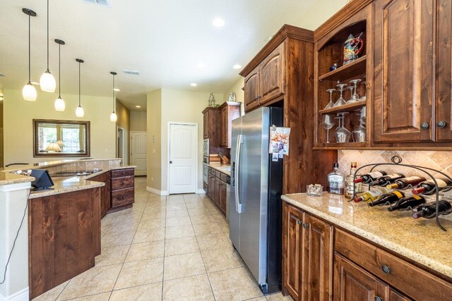 1338 Donovan St, Gonzales, TX 78629 - kitchen with stainless steel fridge with ice dispenser, hanging light fixtures, tasteful backsplash, and light stone countertops