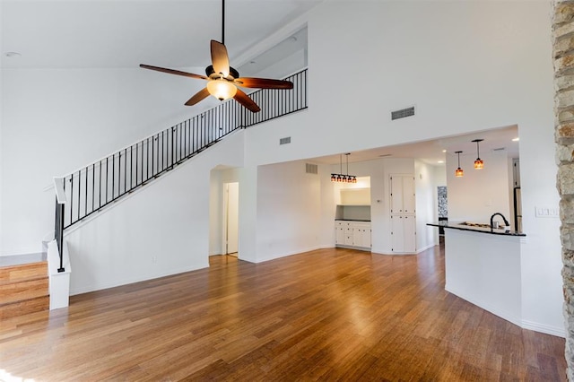 unfurnished living room with ceiling fan, visible vents, wood finished floors, and a high ceiling