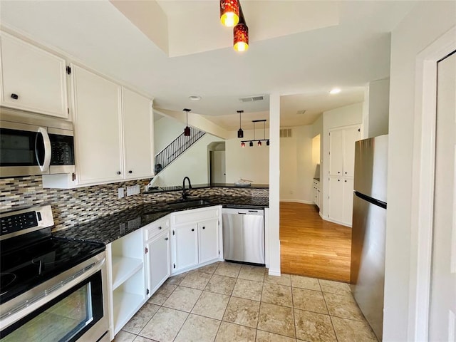 kitchen with light tile patterned floors, a sink, stainless steel appliances, white cabinetry, and decorative light fixtures
