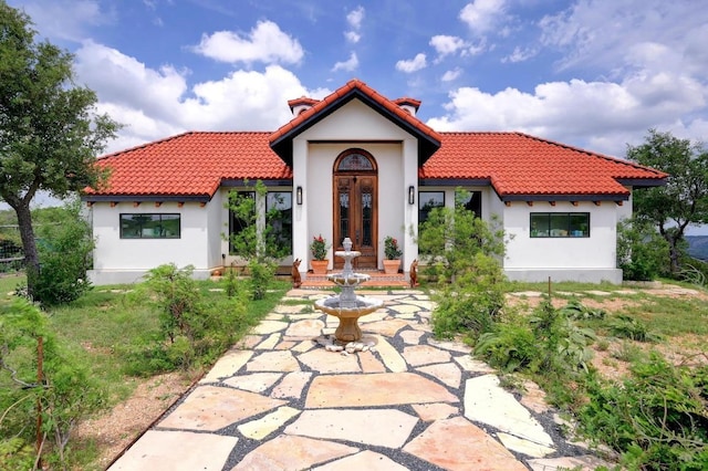 view of front of house featuring french doors, stucco siding, a tile roof, and a chimney