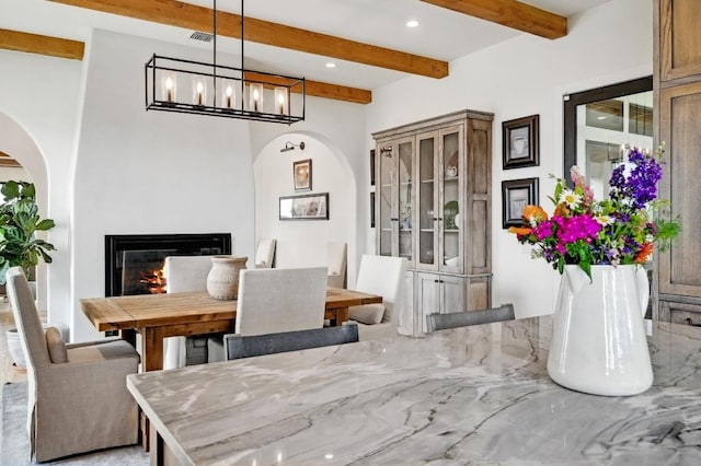 dining area with beam ceiling, recessed lighting, a chandelier, arched walkways, and a glass covered fireplace