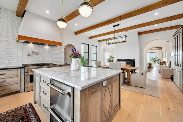 kitchen featuring appliances with stainless steel finishes, decorative backsplash, a kitchen island, arched walkways, and beam ceiling