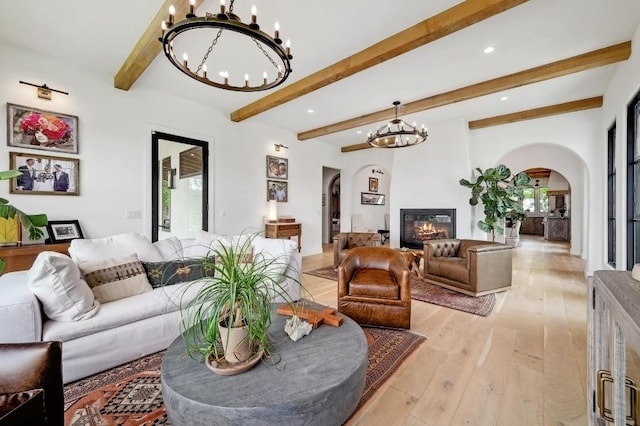 living room featuring a wealth of natural light, arched walkways, beamed ceiling, light wood-style floors, and a chandelier
