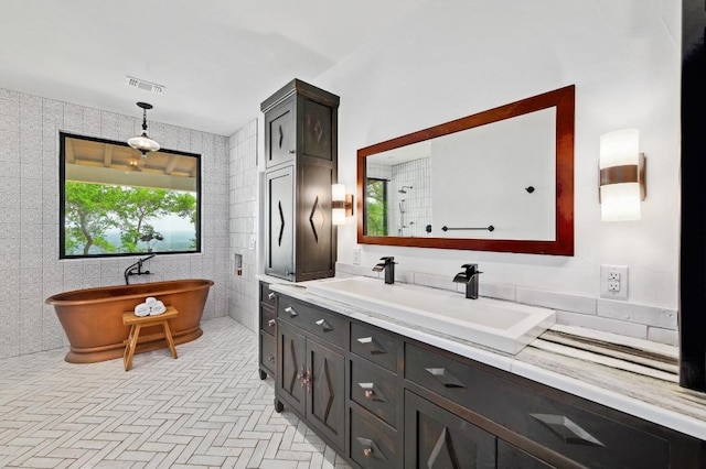 bathroom with tile walls, vanity, visible vents, a soaking tub, and tiled shower