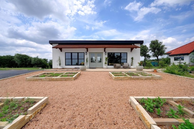 back of house featuring a vegetable garden, stucco siding, and french doors