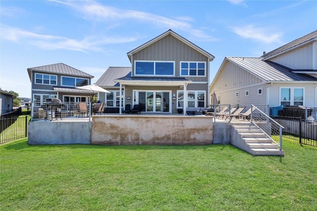 back of property featuring board and batten siding, metal roof, fence private yard, a lawn, and a standing seam roof