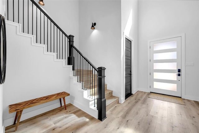 entryway with light wood-type flooring, baseboards, a high ceiling, and stairs