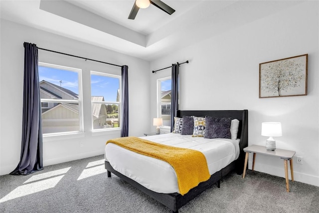 bedroom with a raised ceiling, carpet floors, baseboards, and a ceiling fan