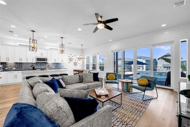 living room featuring ceiling fan with notable chandelier, light wood-type flooring, and visible vents