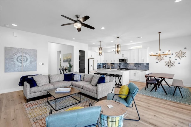 living area with a chandelier, ceiling fan, light wood-type flooring, baseboards, and recessed lighting