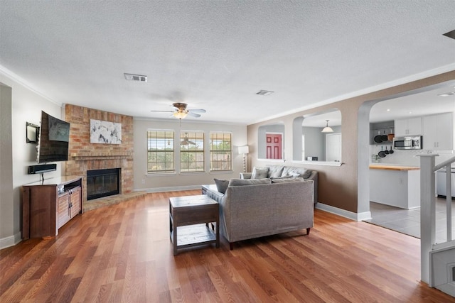 living area with ceiling fan, a brick fireplace, visible vents, and light wood-style floors
