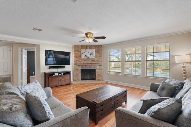 living room featuring a fireplace, light wood-type flooring, visible vents, a textured ceiling, and ceiling fan