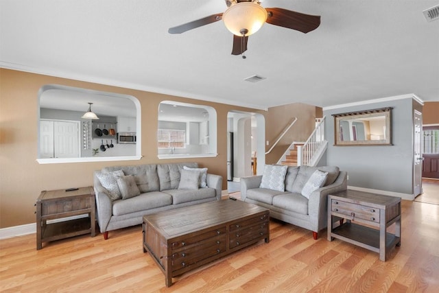 living room featuring a ceiling fan, baseboards, arched walkways, light wood-style floors, and stairs
