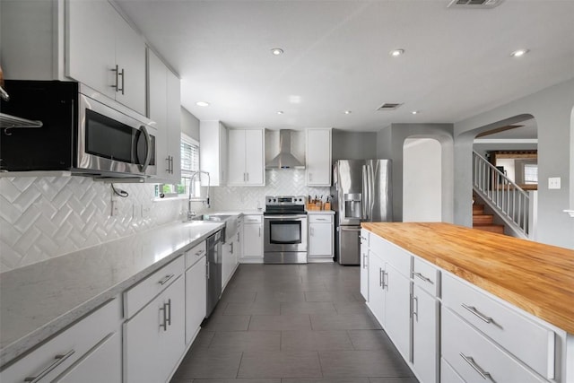 kitchen featuring wall chimney exhaust hood, visible vents, arched walkways, backsplash, and appliances with stainless steel finishes