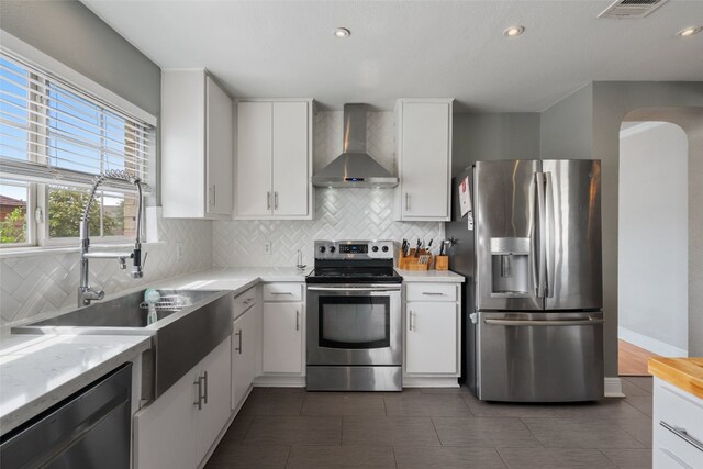 kitchen featuring a sink, wall chimney exhaust hood, light countertops, and appliances with stainless steel finishes