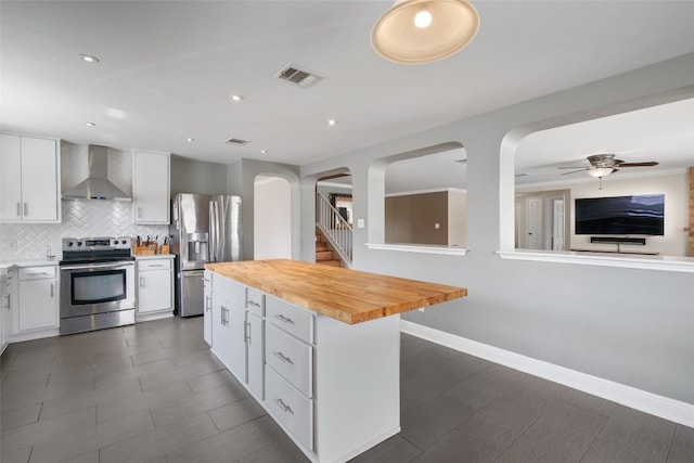kitchen featuring visible vents, wood counters, wall chimney exhaust hood, arched walkways, and appliances with stainless steel finishes