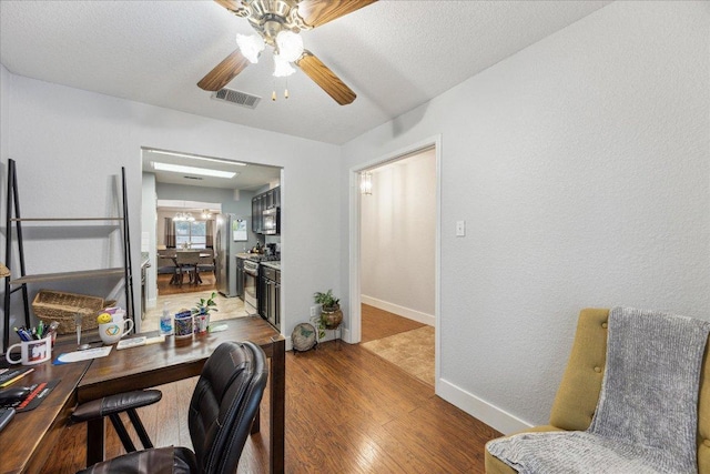 office featuring a textured ceiling, baseboards, ceiling fan, visible vents, and wood finished floors