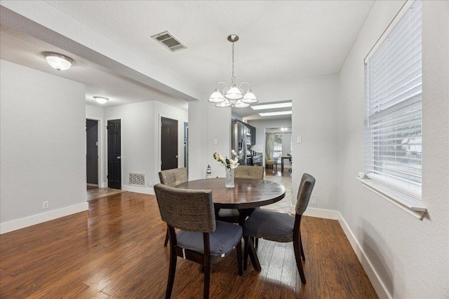 dining area featuring a notable chandelier, baseboards, visible vents, and wood finished floors