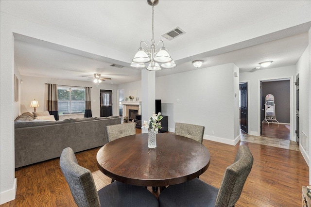 dining area featuring baseboards, visible vents, ceiling fan with notable chandelier, wood finished floors, and a fireplace