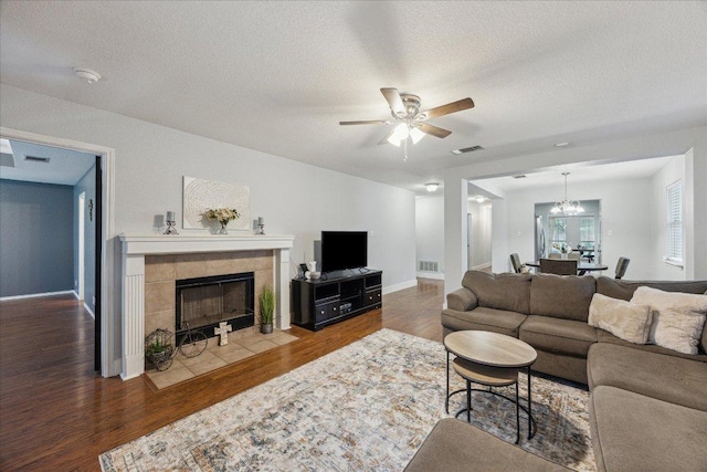 living room featuring ceiling fan with notable chandelier, wood finished floors, a textured ceiling, visible vents, and a fireplace