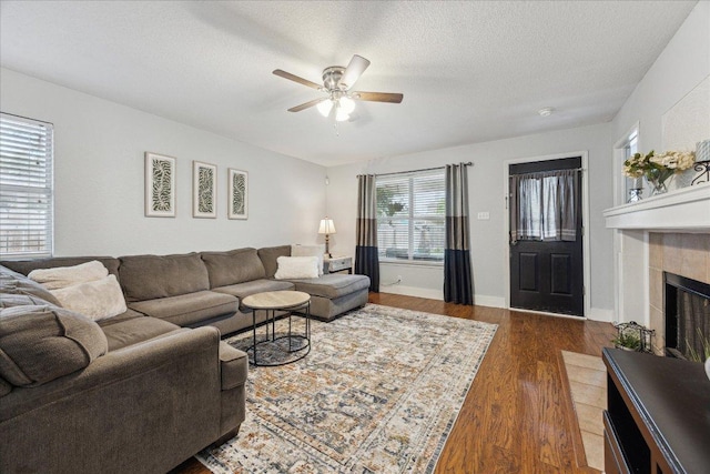 living area with a textured ceiling, baseboards, ceiling fan, a tile fireplace, and dark wood-style floors