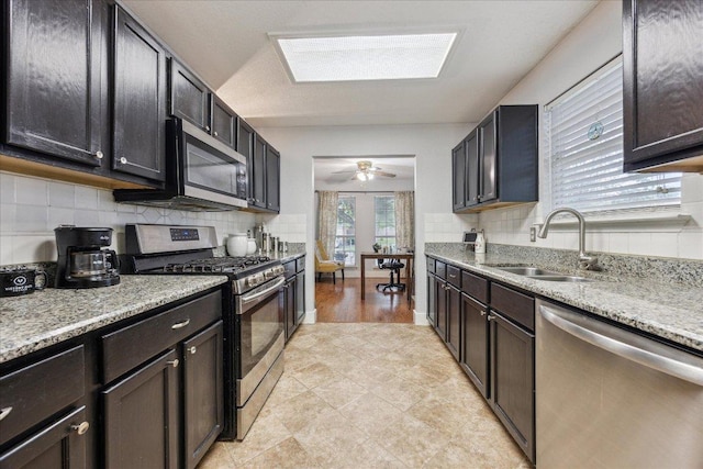 kitchen with light stone countertops, ceiling fan, a sink, decorative backsplash, and stainless steel appliances