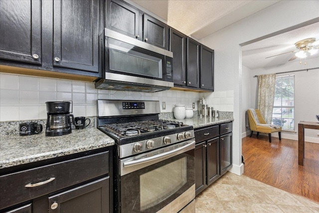 kitchen featuring a ceiling fan, light stone counters, dark cabinets, stainless steel appliances, and tasteful backsplash