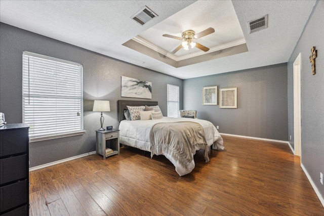 bedroom featuring crown molding, a raised ceiling, visible vents, and wood finished floors